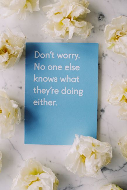 A light blue rectangular card with white text reading 'Don't worry. No one else knows what they're doing either.' is positioned on a white marble surface with grey veining. Surrounding the card are sc