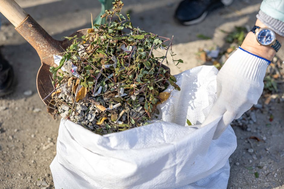 A black residential waste bin placed on the pavement beside a curbside street at night, with its lid open revealing assorted rubbish including paper, cardboard, and plastic items. The bin is marked wi